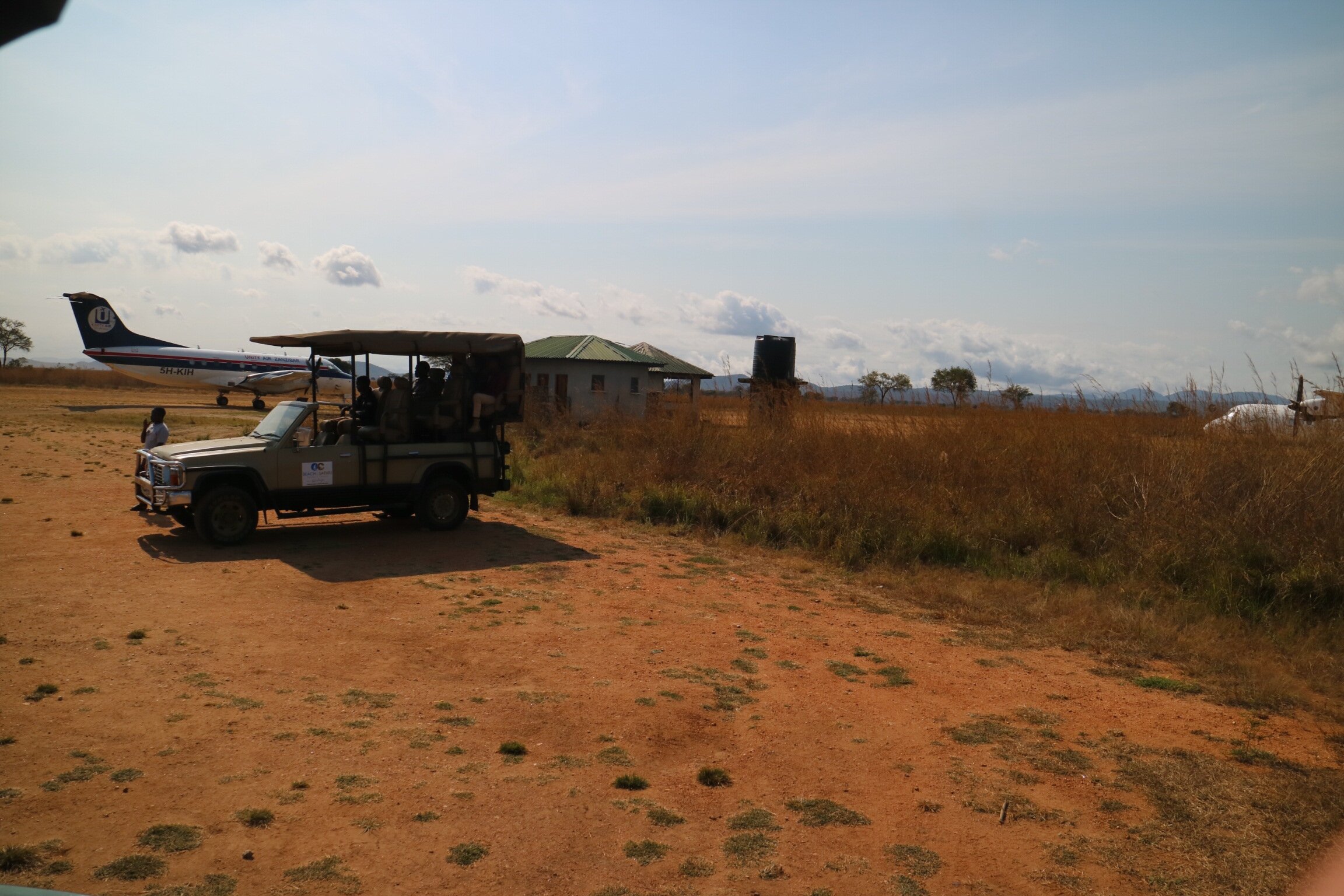 Safari vehicle with guests beside the airstrip and a light aircraft in Mikumi National Park