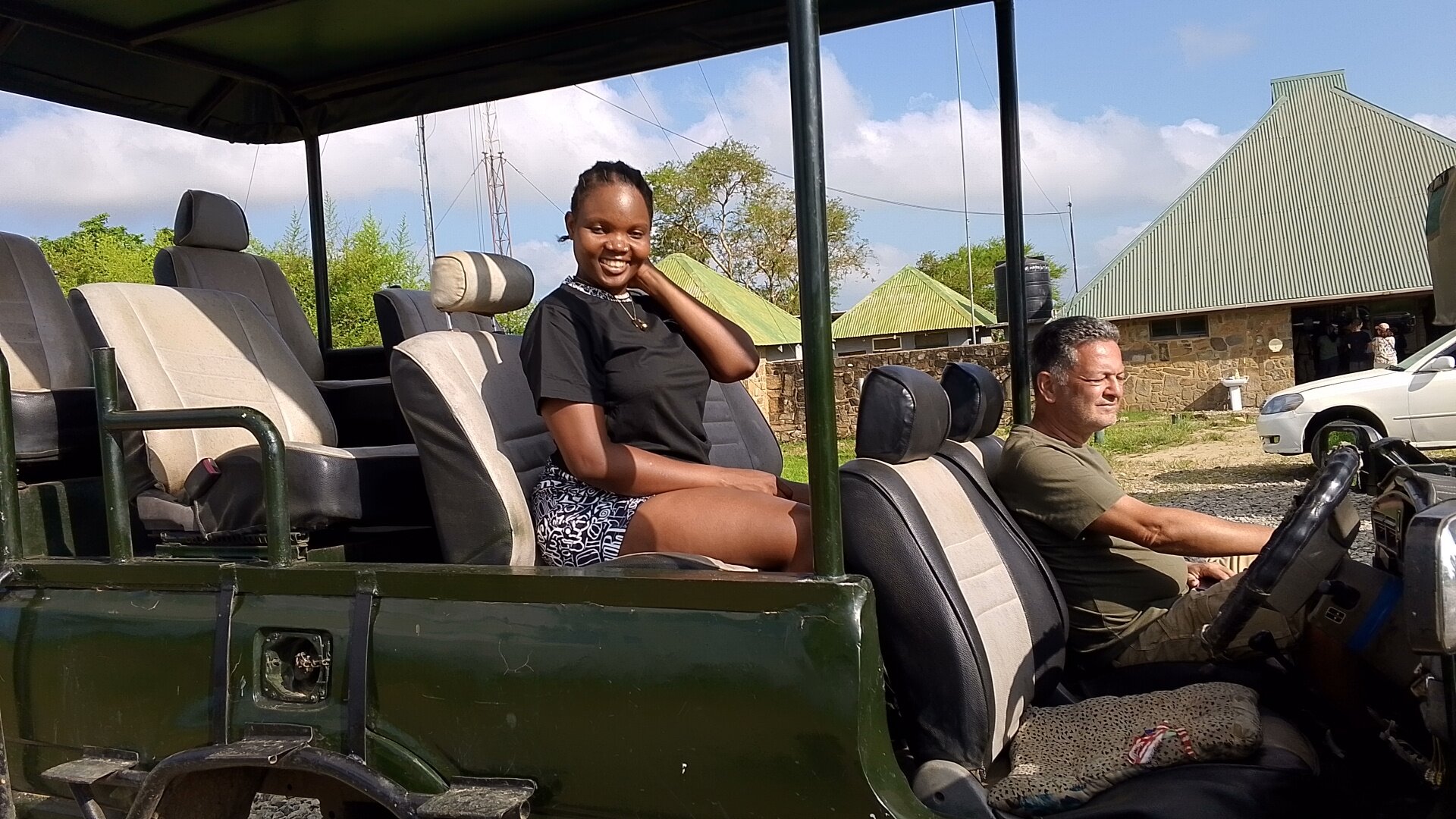 Smiling guest and driver in open safari truck at park buildings