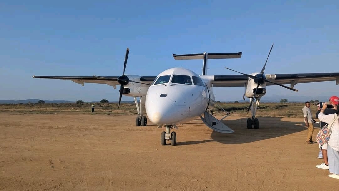 A twin propeller plane parked on the dirt airstrip at Mikumi
