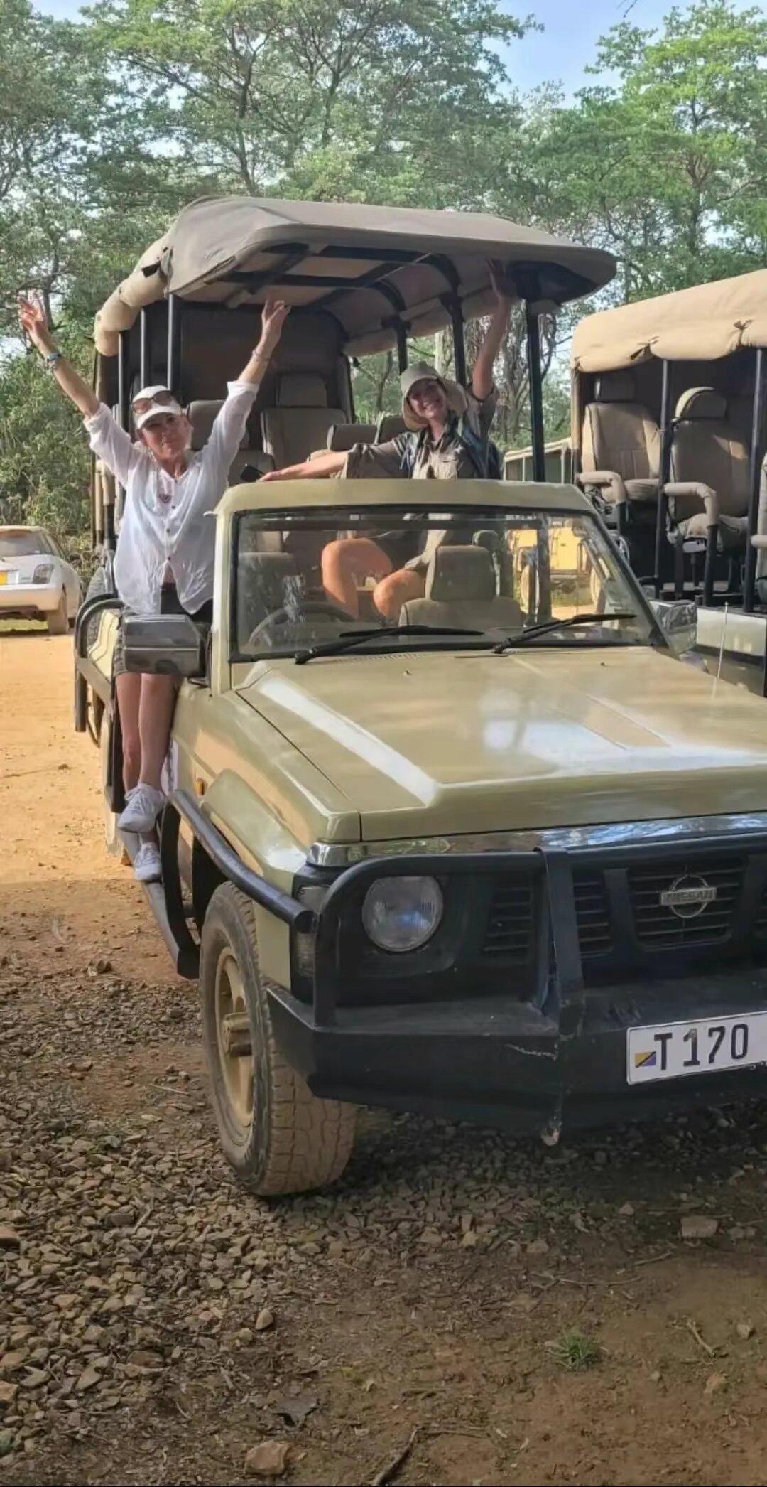 Two guests waving from a cream open safari vehicle in Mikumi National Park